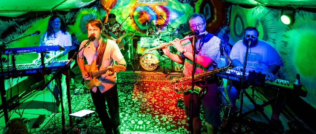 Wurk plays under a tent lit with green stage lights and decorated with tie-dye.
